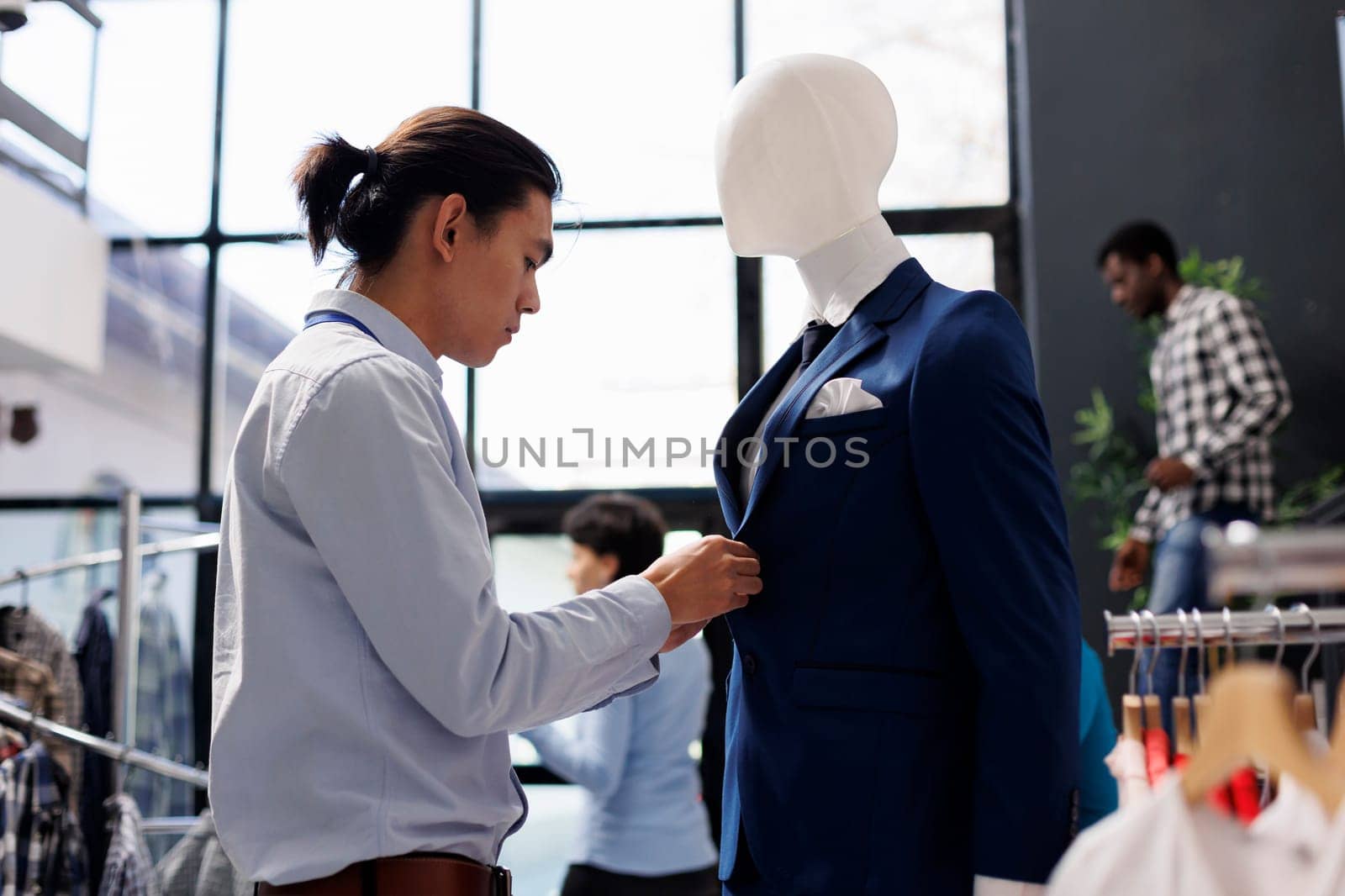 Asian worker arranging mannequin with formal suit, working at store visual with fashionable merchandise. Employee preparing boutique for opening, waiting for customers in shopping centre