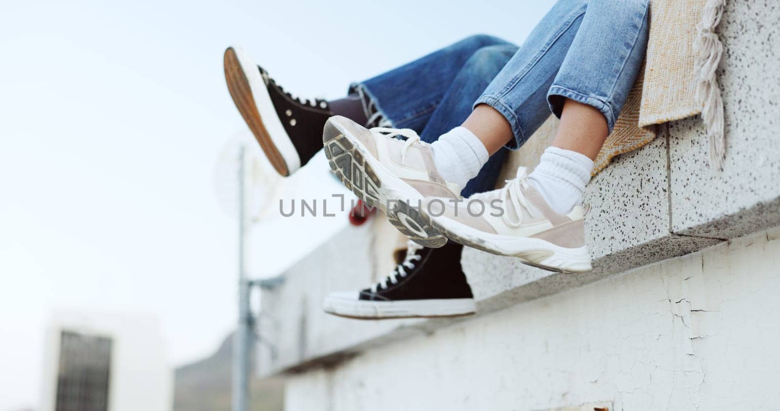 Shoes, legs and couple on rooftop in the city sitting together, have fun and bonding. Fashion sneakers, style and friends kick feet on building edge, enjoy weekend, freedom and holiday in urban town by YuriArcurs