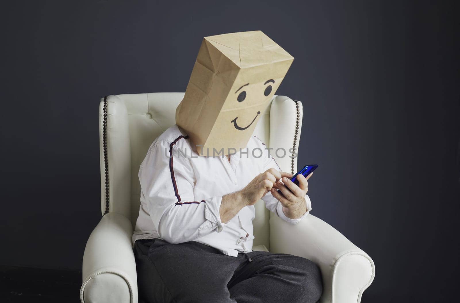 A man in a white shirt with a paper bag on his head, with a smiley face drawn, talking on the phone.