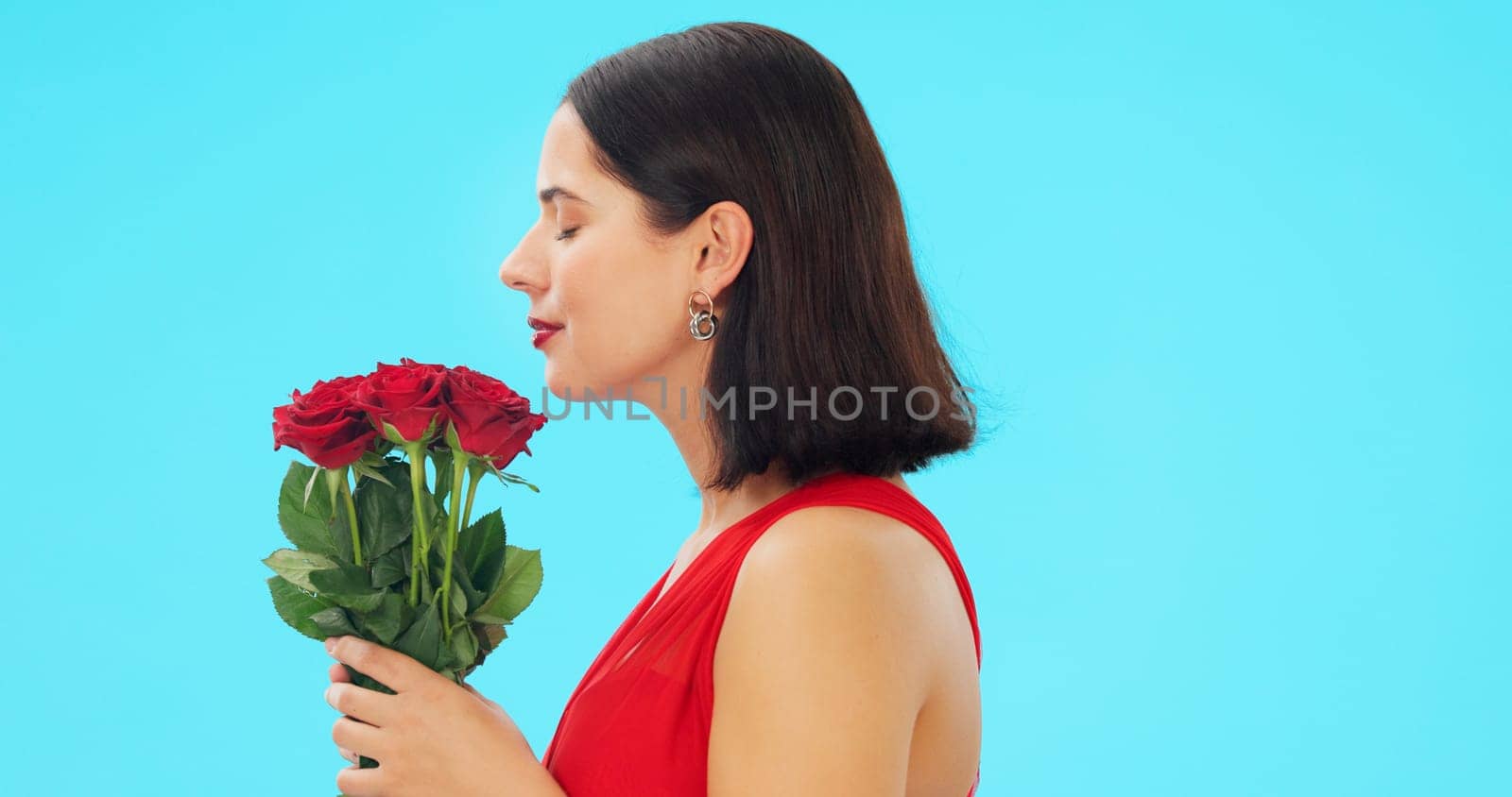 Rose, smell and face of woman in studio with floral bouquet in celebration of love, romance or valentines day. Portrait, scent and girl happy, smile and excited for flowers against blue background.