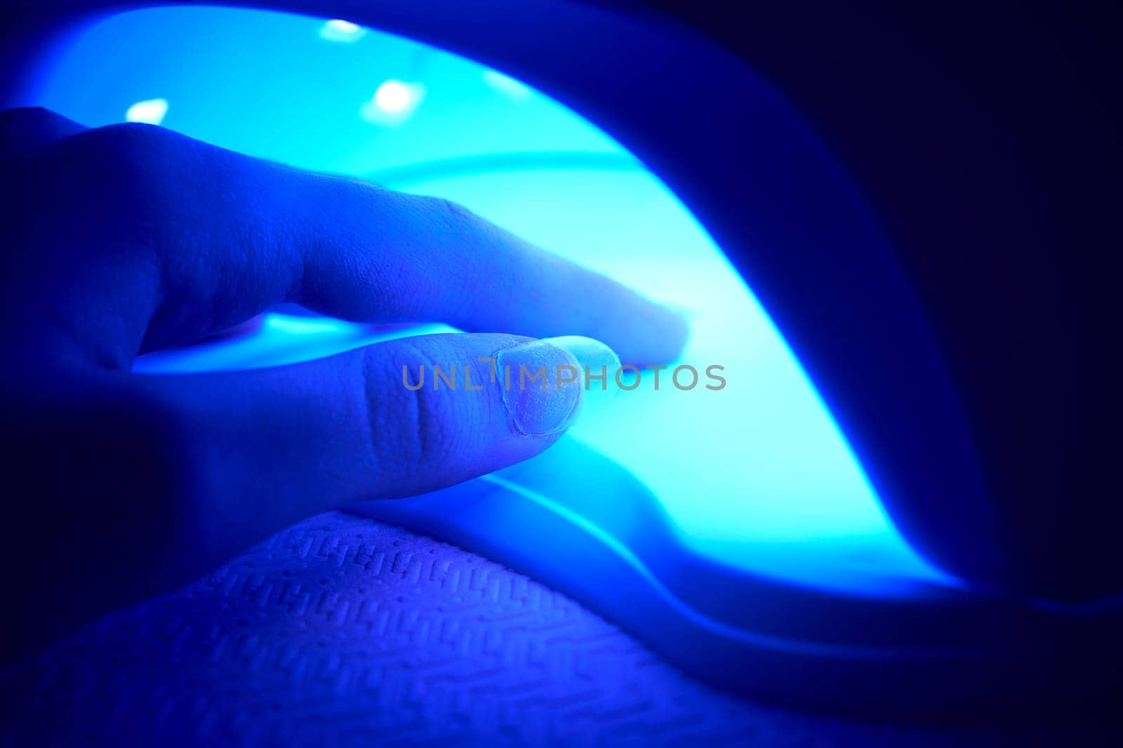 Close-up of a woman's hand under an ultraviolet lamp. Gel polish for nails. Beauty salon and beautician appointment concept
