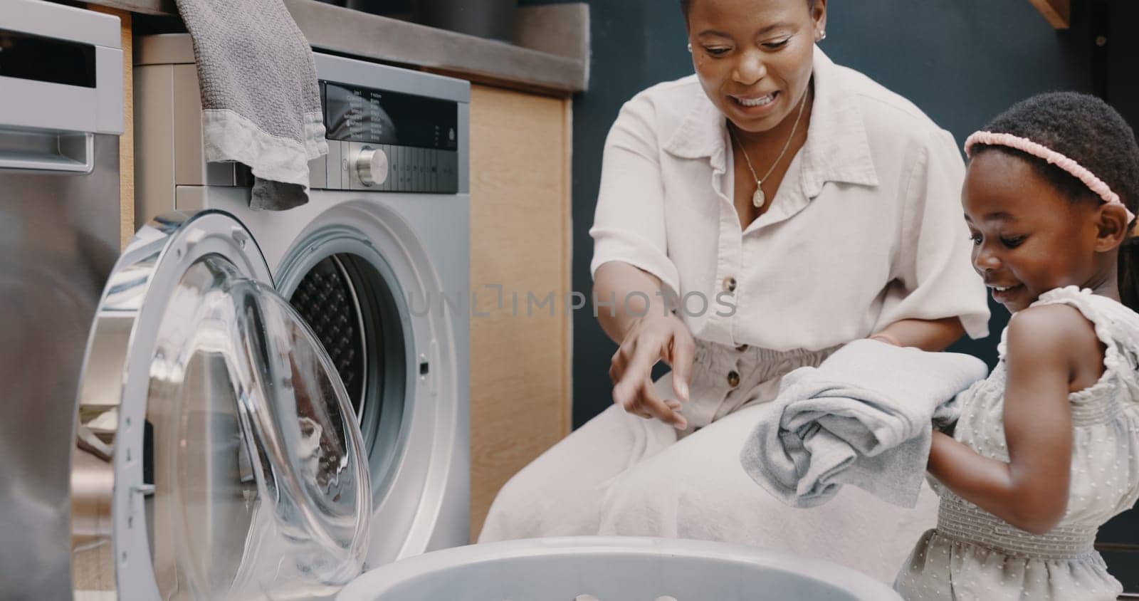 Laundry, mother and child helping with folding of clothes together in a house. Happy, excited and young girl giving help to her mom while cleaning clothing from a washing machine in their home by YuriArcurs