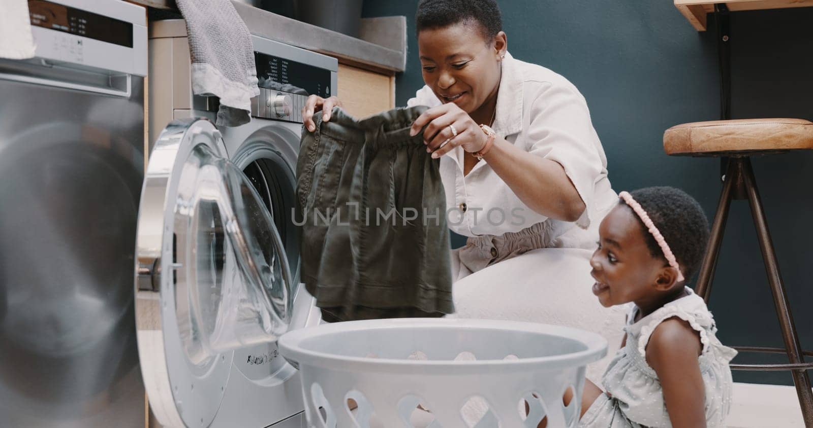 Laundry, mother and child helping with folding of clothes together in a house. Happy, excited and young girl giving help to her mom while cleaning clothing from a washing machine in their home by YuriArcurs