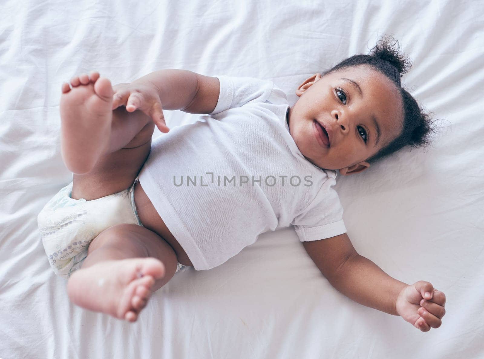 Happy baby, portrait and girl on a bedroom bed relax and calm in a nursery after rest. Young newborn, child and kid with a diaper in the morning with wellbeing and childcare from above in a house.