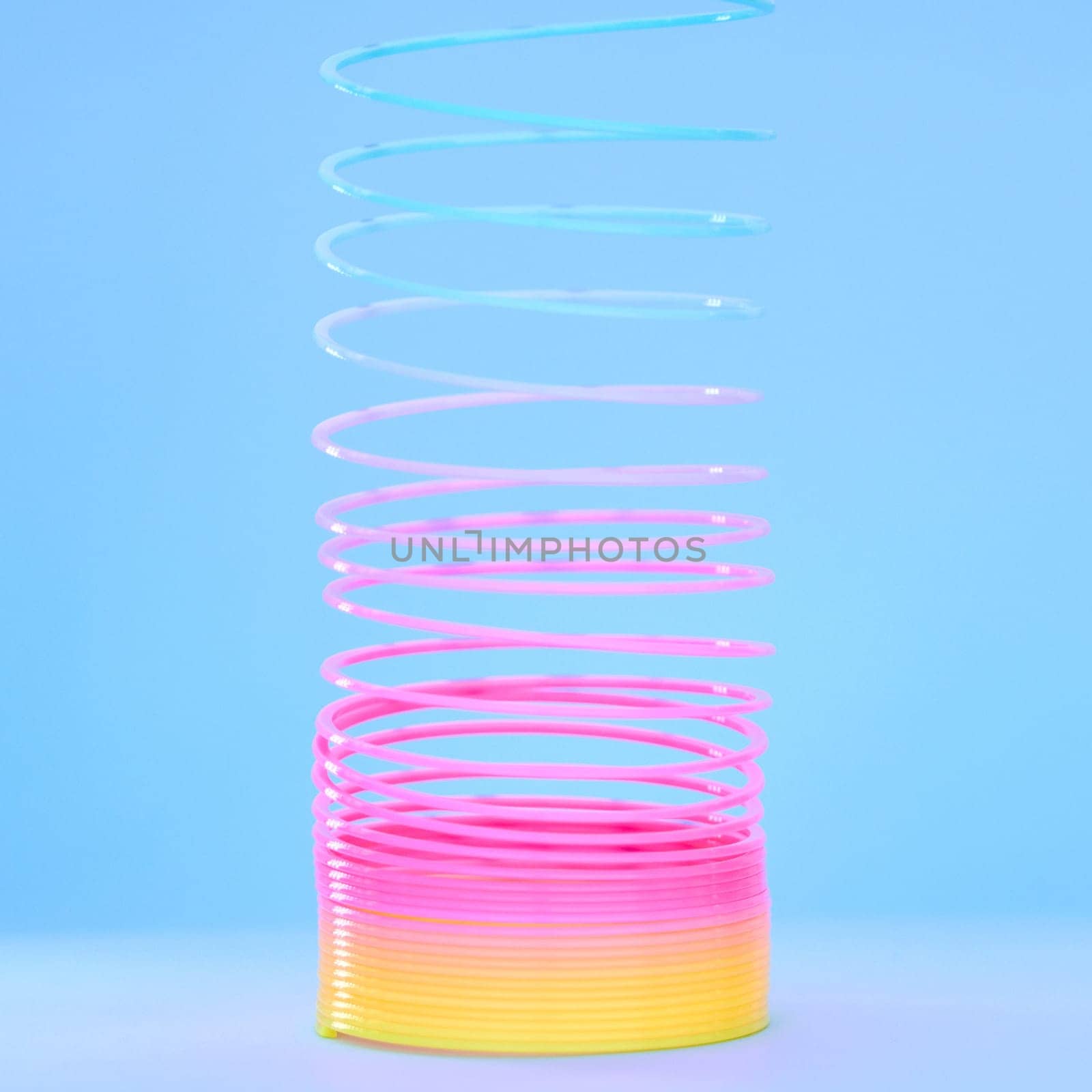 Rainbow slinky toy, spring and plastic product in studio isolated against a blue background mockup. Flexible toys, colorful spirals and childhood item stretched out for playing, having fun and games