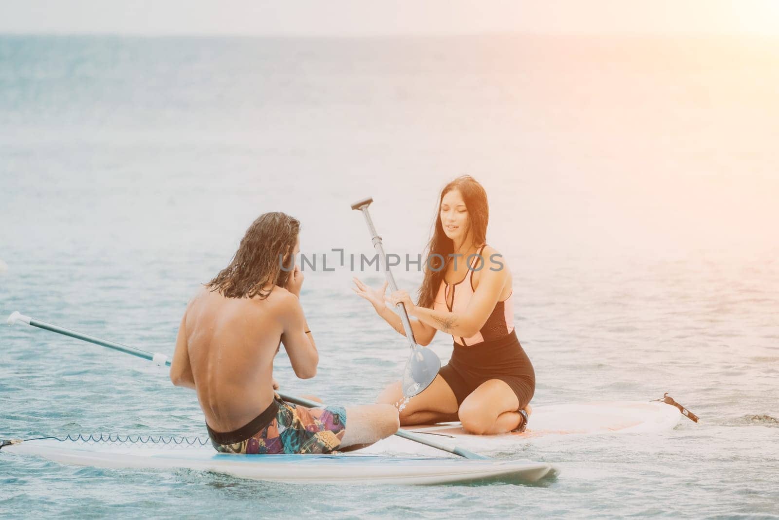 Sea woman and man on sup. Silhouette of happy young woman and man, surfing on SUP board, confident paddling through water surface. Idyllic sunset. Active lifestyle at sea or river. by panophotograph