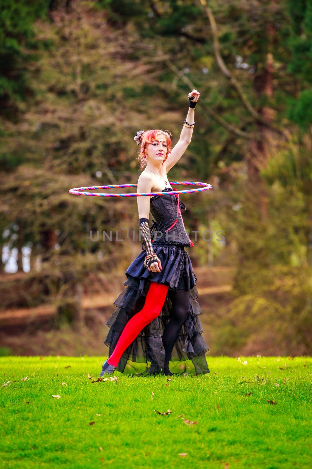 Young beautiful woman in circus costume play with hula hoop in the park.