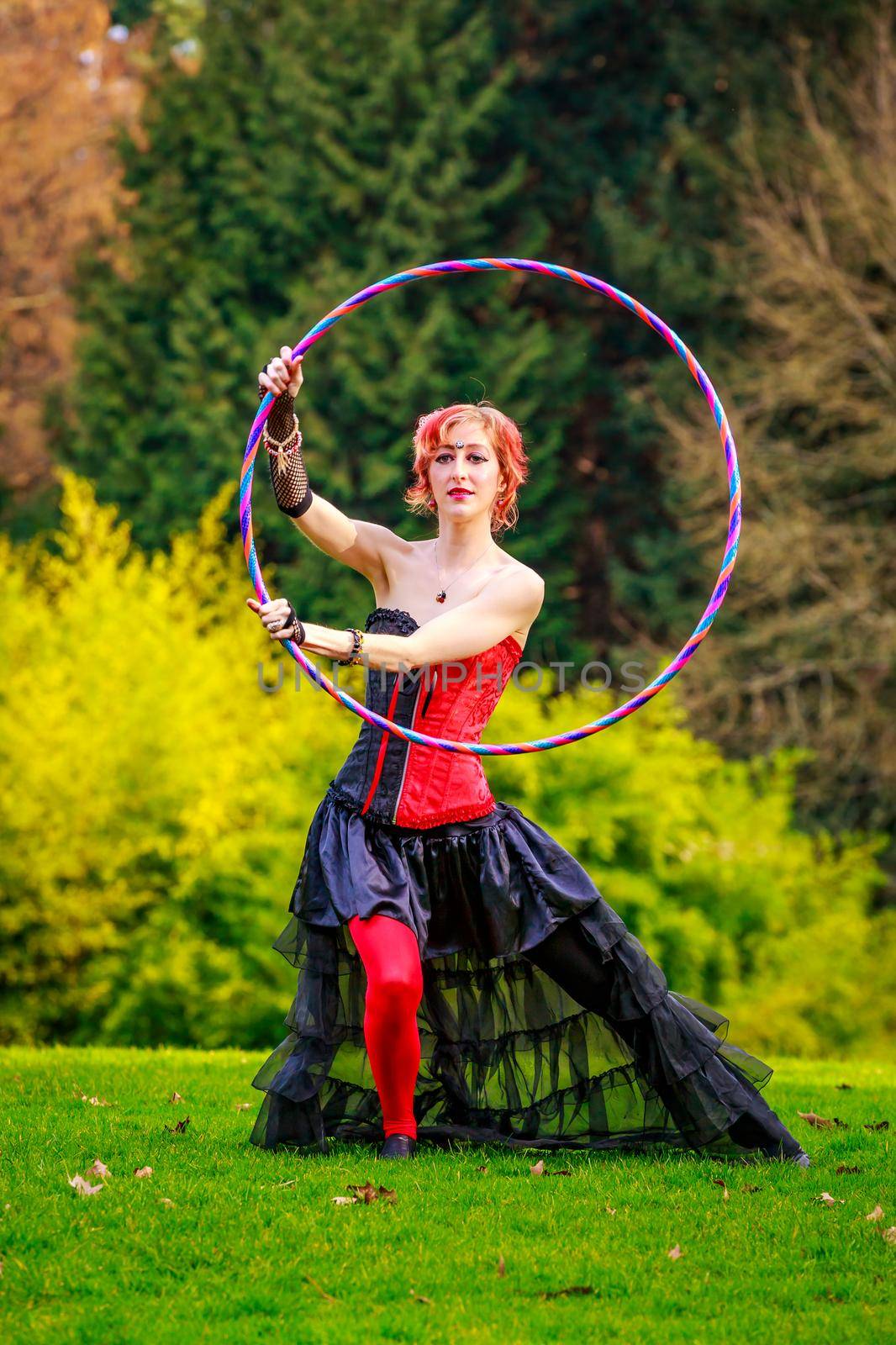 Young beautiful woman in circus costume play with hula hoop in the park.