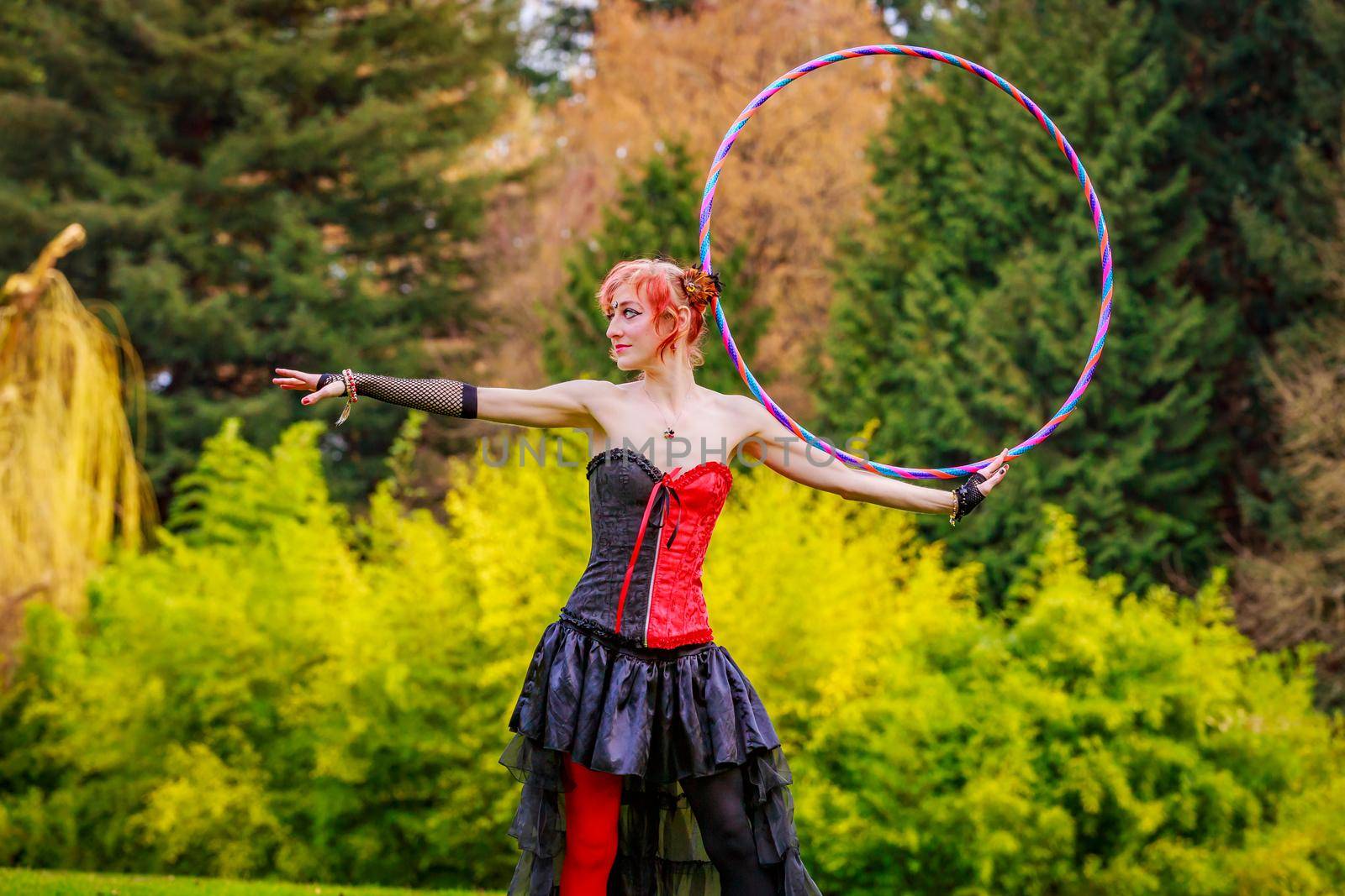 Young beautiful woman in circus costume play with hula hoop in the park.