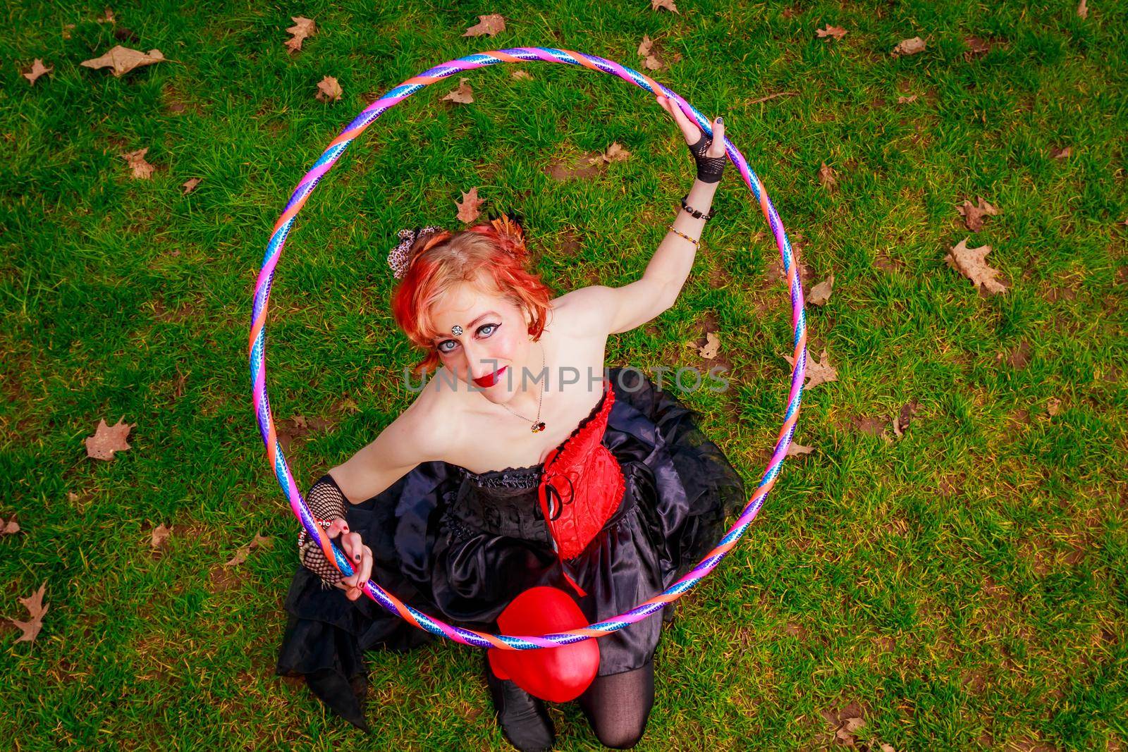 Young beautiful woman in circus costume play with hula hoop in the park.