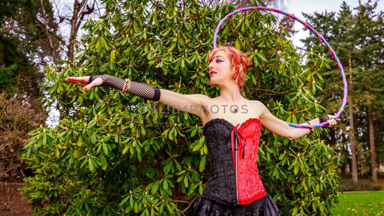 Young beautiful woman in circus costume play with hula hoop in the park.