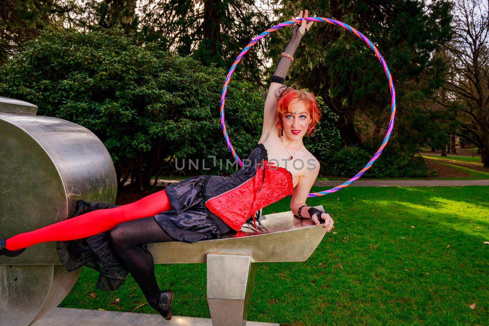 Young beautiful woman in circus costume play with hula hoop in the park.