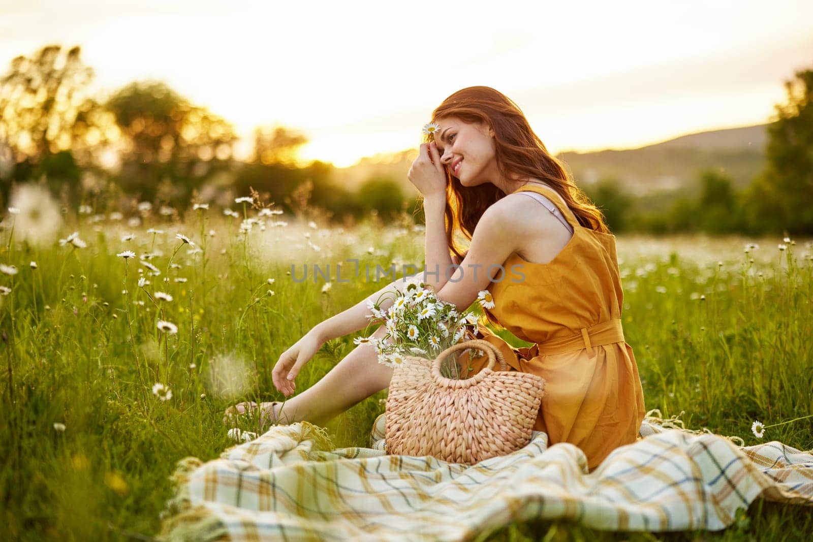 beautiful, happy woman in an orange dress is resting sitting on a plaid in a chamomile field by Vichizh