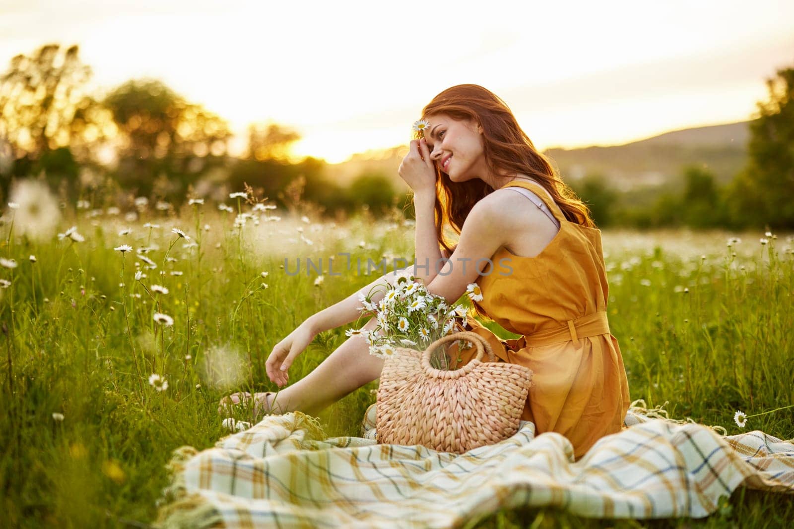 beautiful, happy woman in an orange dress is resting sitting on a plaid in a chamomile field. High quality photo