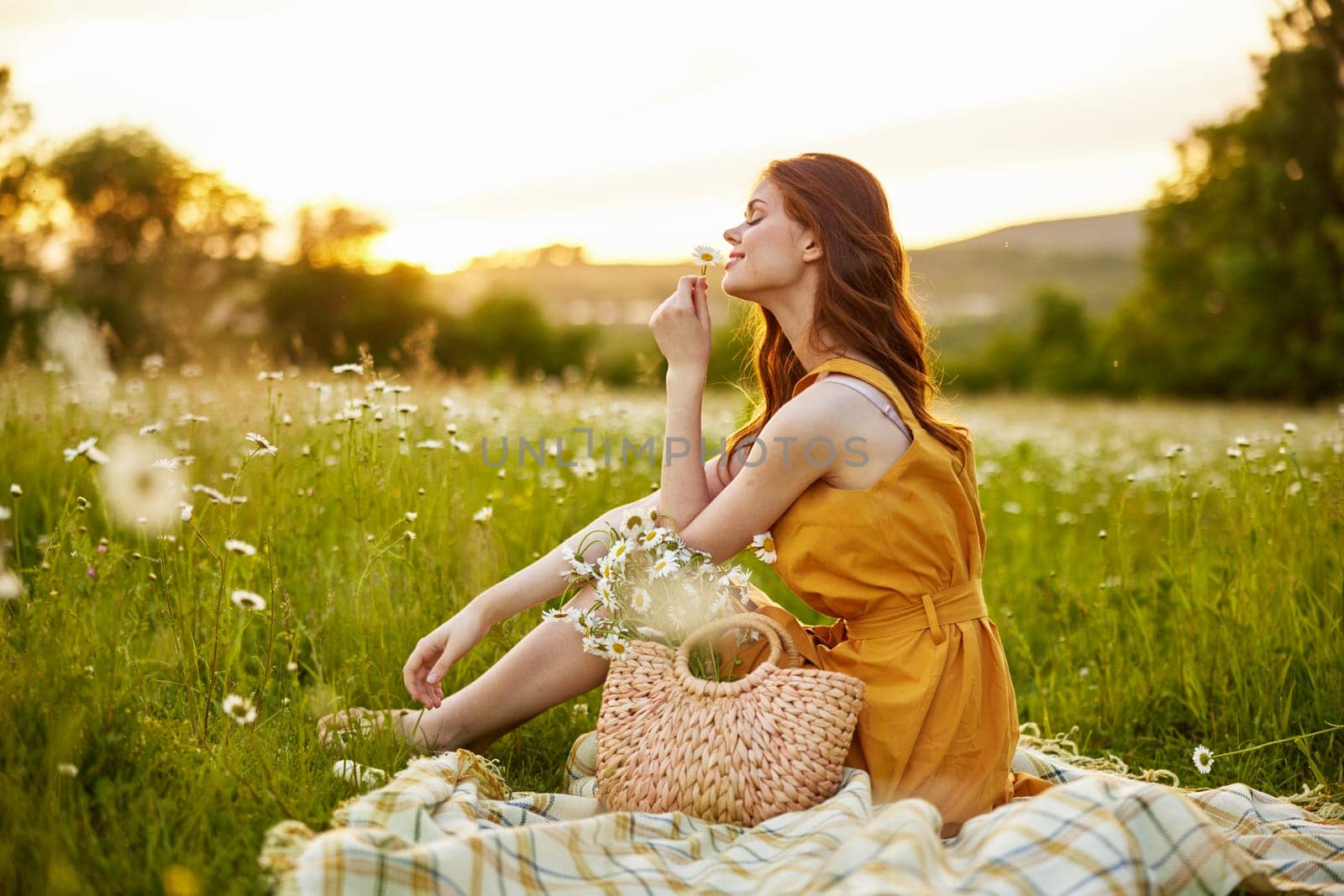 beautiful, happy woman in an orange dress is resting sitting on a plaid in a chamomile field. High quality photo