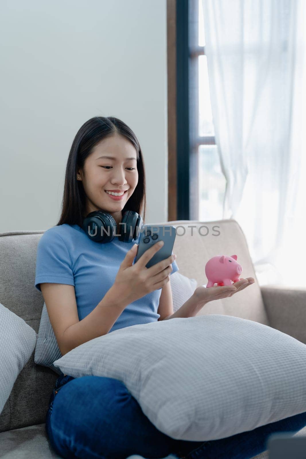 Asian young woman holding a piggy bank and using smartphone mobile, Savings concepts. by Manastrong