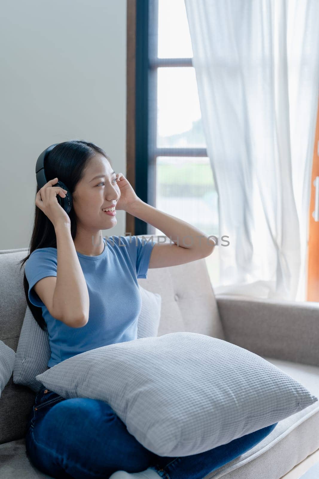 Peaceful girl in modern wireless headphones sit relax on comfortable couch listening to music, on cozy sofa, stress free concept