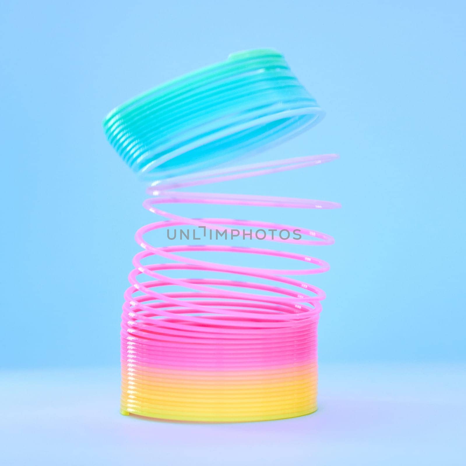 Rainbow slinky toy, spring and plastic product in studio isolated against a blue background mockup. Flexible toys, colorful spirals and childhood item stretched out for playing, having fun and games