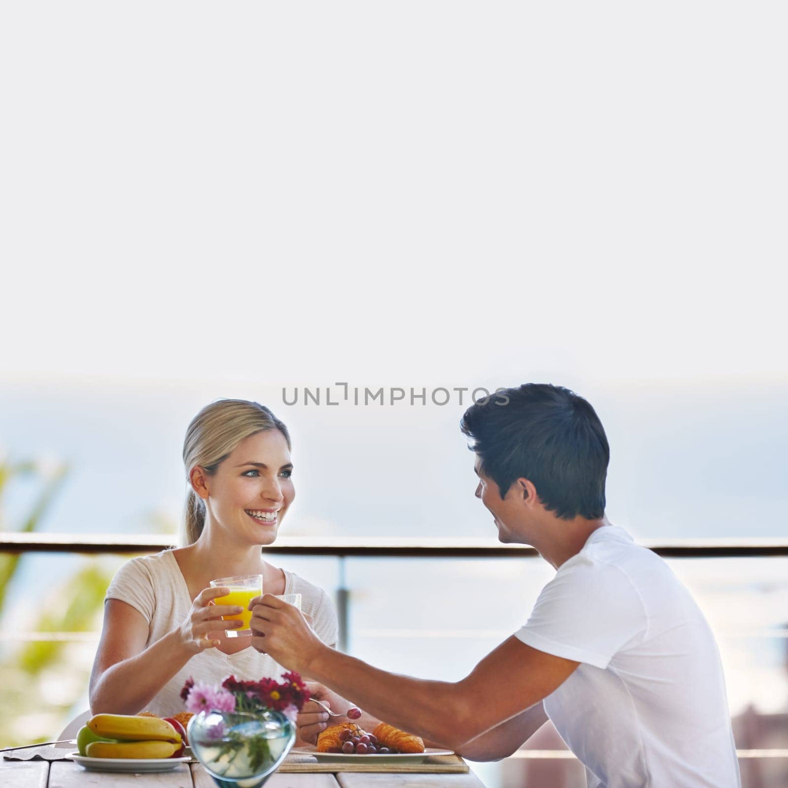 Getting in their daily serving of love. a happy young couple eating breakfast together on the deck at home. by YuriArcurs