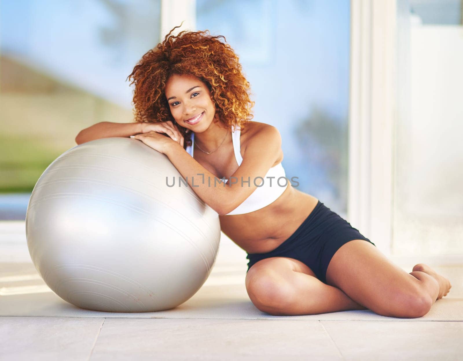 Fit is the only way to go. a young woman leaning against her exercise ball. by YuriArcurs