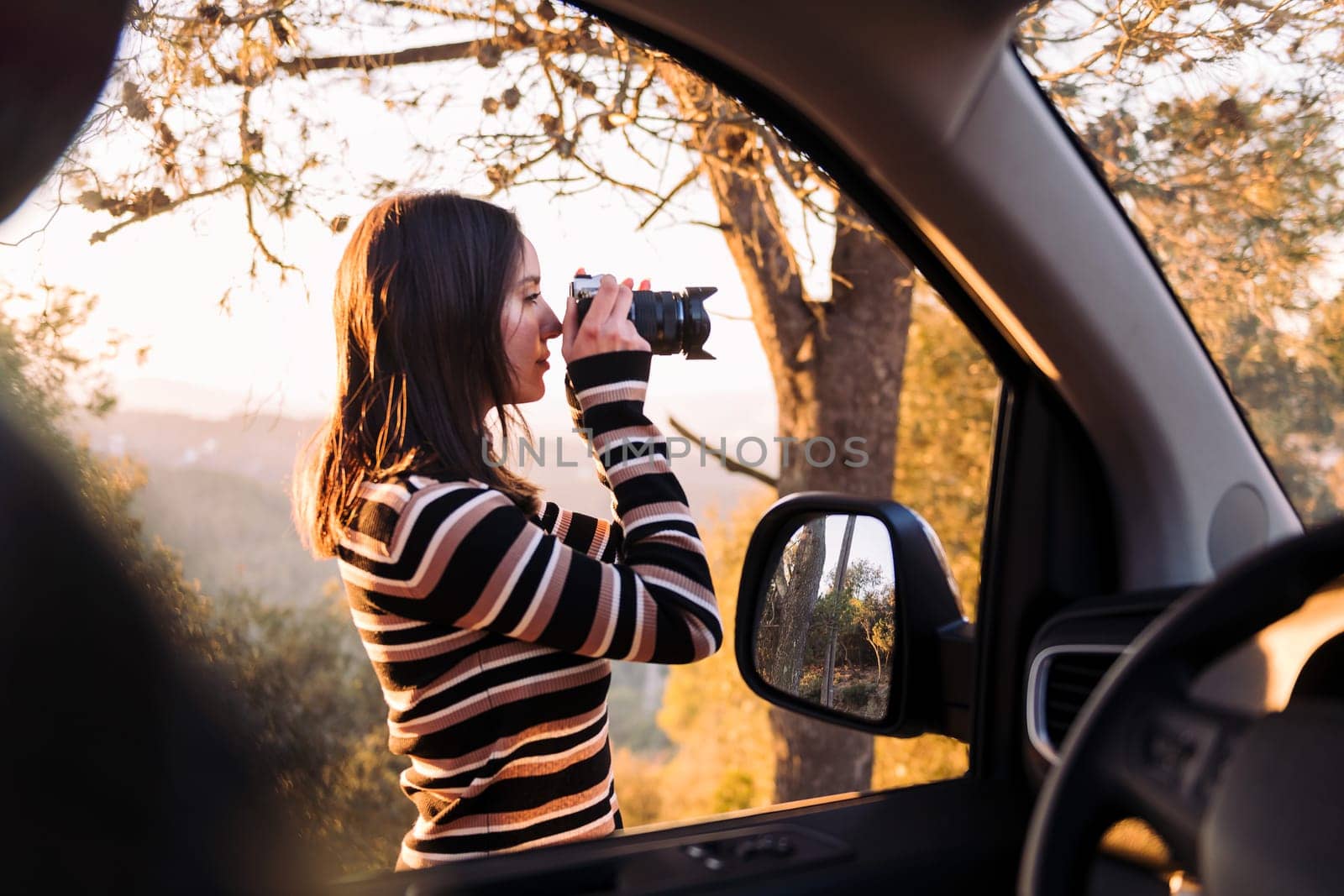 young caucasian woman taking photos of nature with a camera during a road trip in camper van, concept of van life and travel adventures