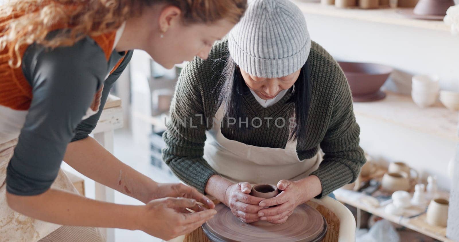 Pottery teacher, studio and workshop learning, training and teaching to seniorwoman on craft wheel for creativity, clay and sculpture process. Artist helping student in class, design and creative mol.