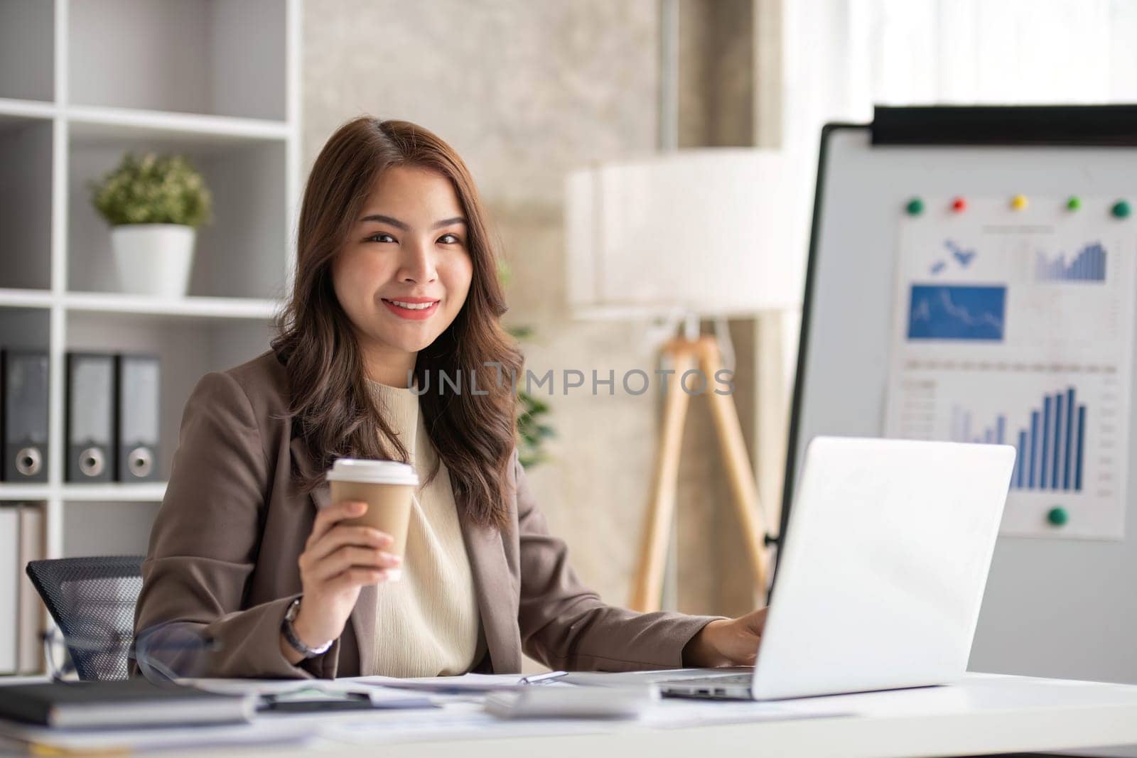 Cheerful business lady working on laptop in office, Asian happy beautiful businesswoman in formal suit work in workplace. Attractive female employee office worker smile...