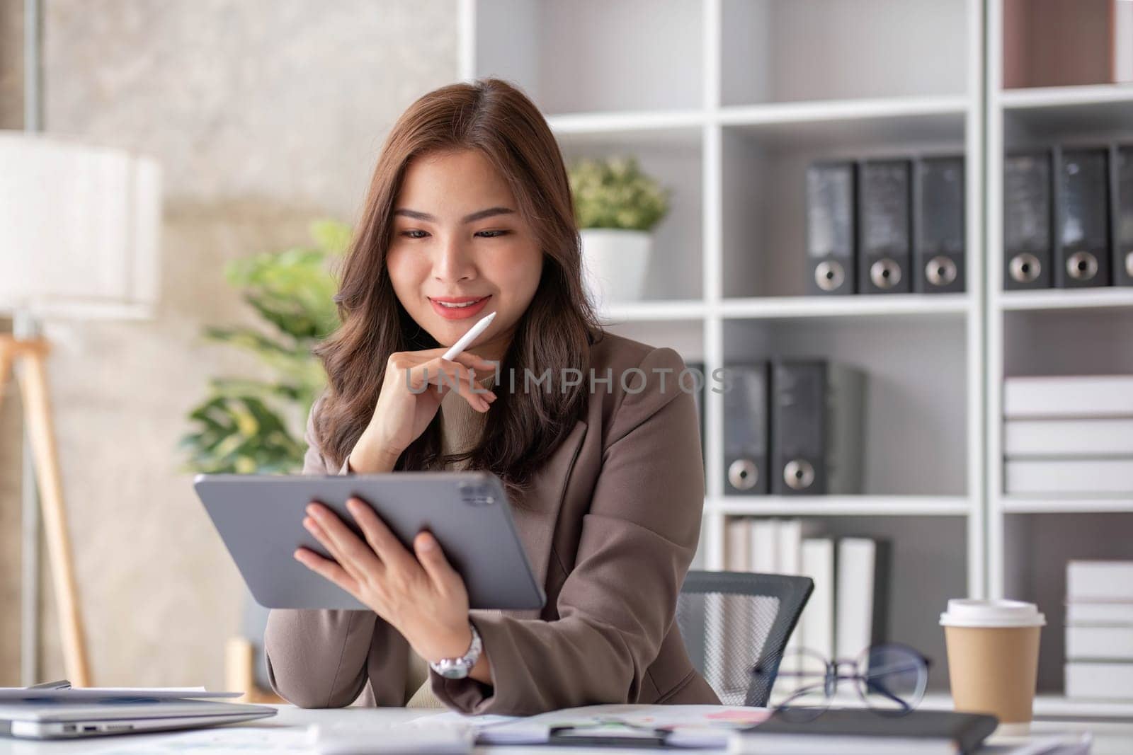 Cheerful business lady working on laptop in office, Asian happy beautiful businesswoman in formal suit work in workplace. Attractive female employee office worker smile...