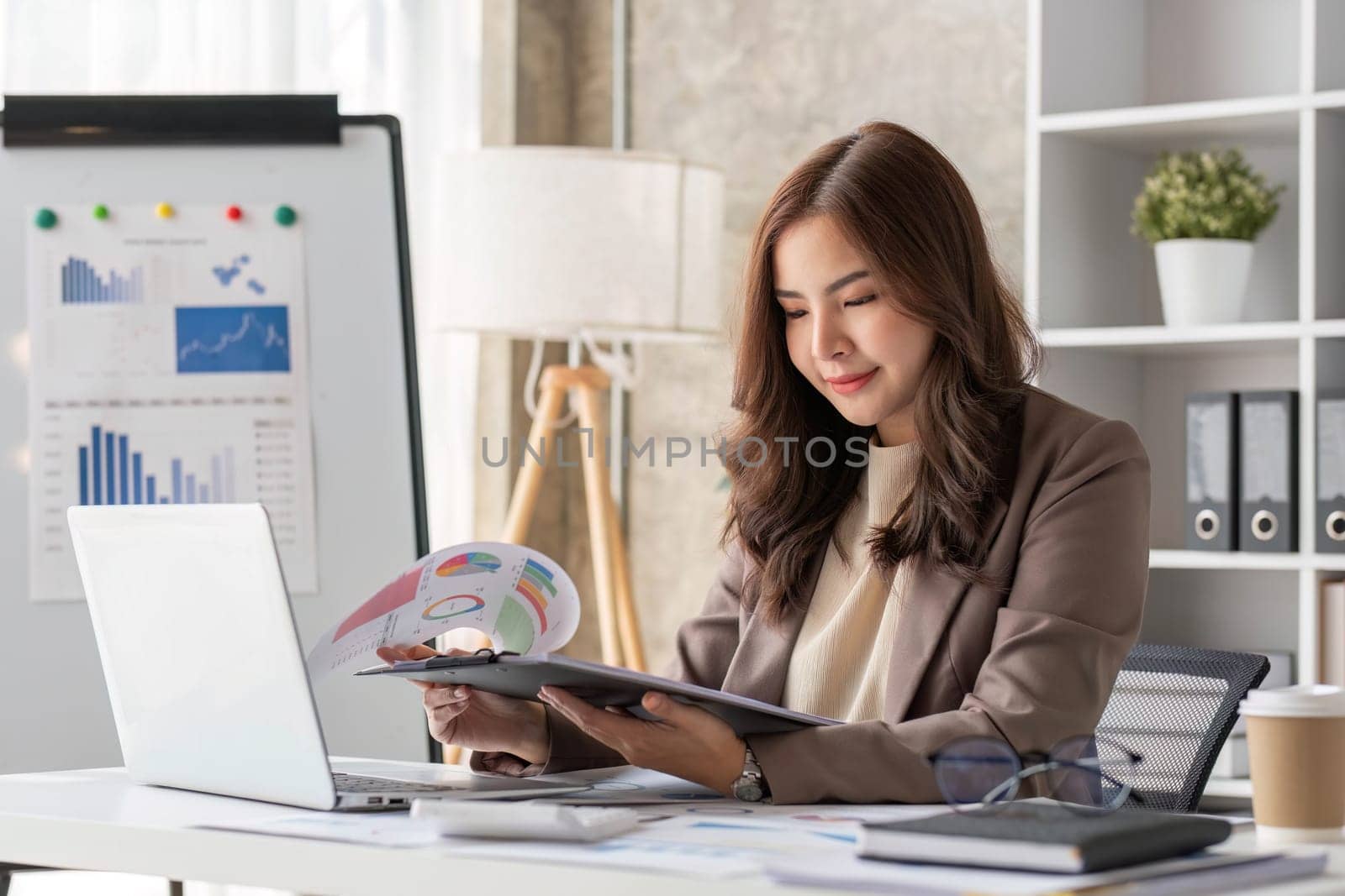 Cheerful business lady working on laptop in office, Asian happy beautiful businesswoman in formal suit work in workplace. Attractive female employee office worker smile...