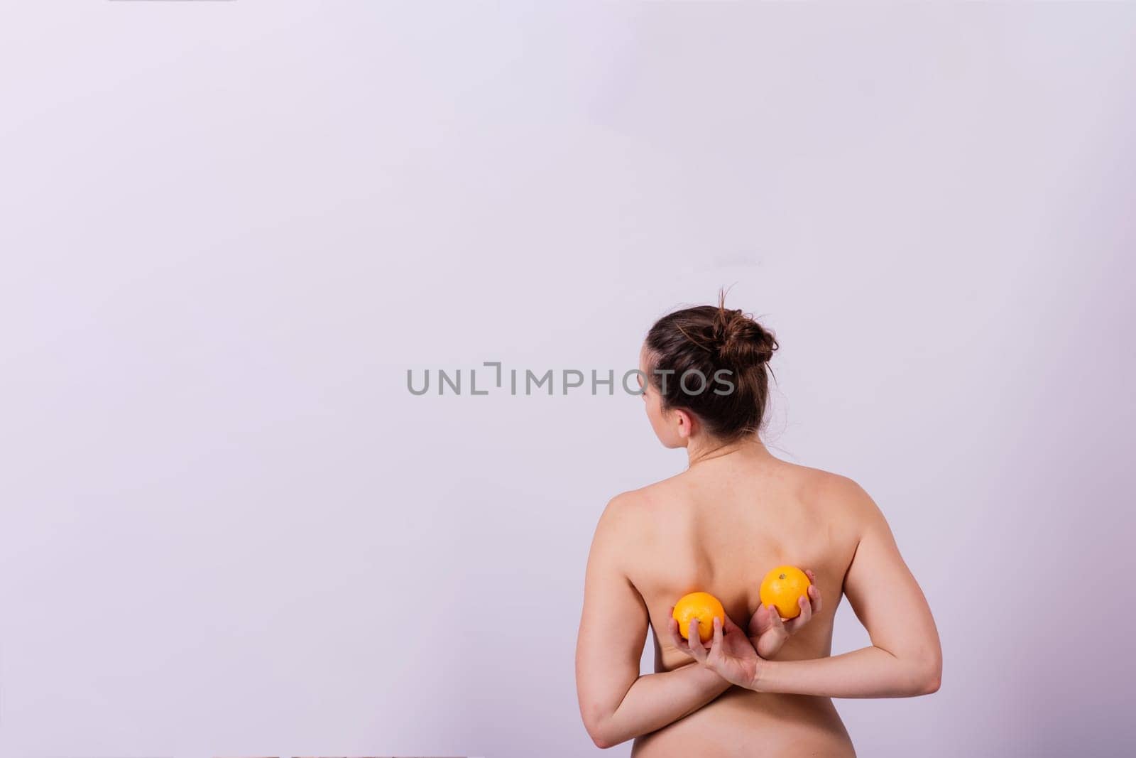 Slim woman is holding orange. Perfect female back without any cellulite.