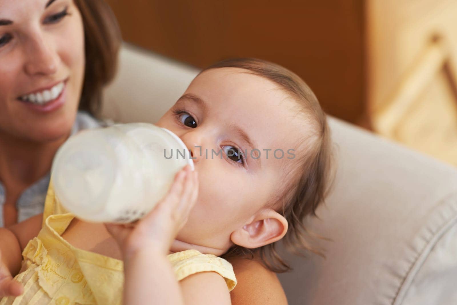 Somebodys thirsty. Closeup portrait of a baby girl sitting on her moms lap and drinking from a baby bottle. by YuriArcurs