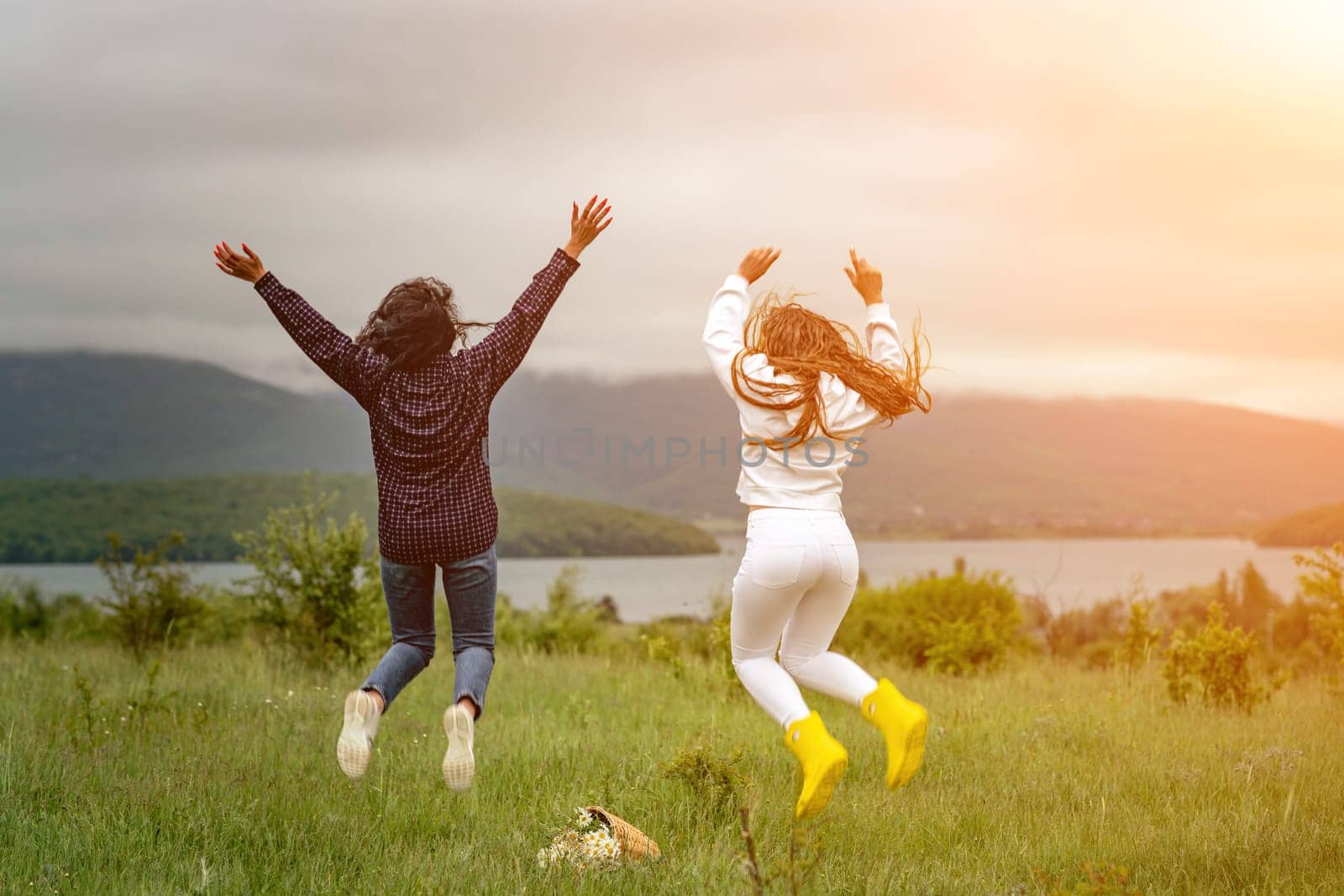 Two girls with long hair are jumping in a clearing overlooking the mountains. The concept of travel and tourism to different countries. by Matiunina