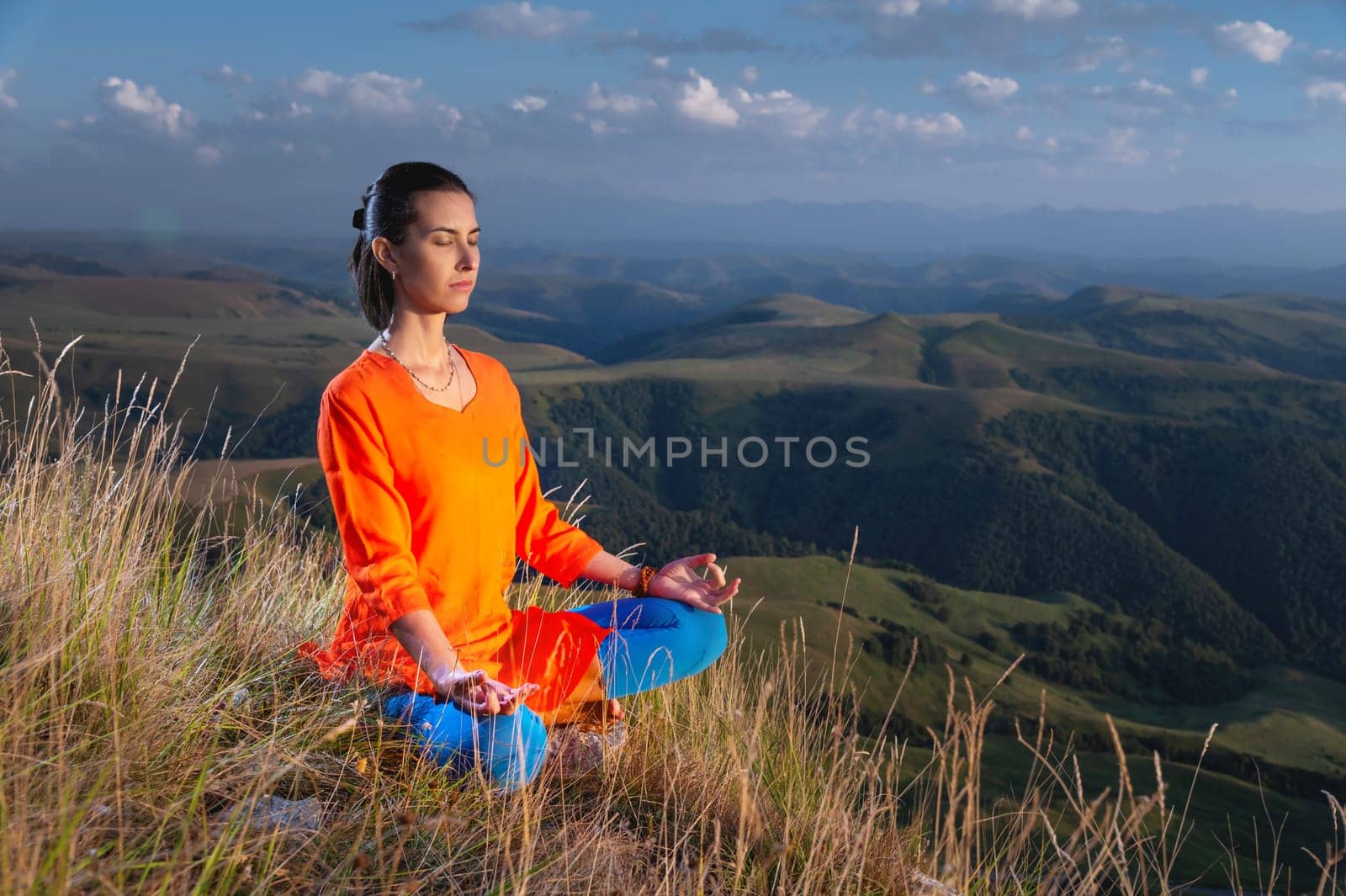 woman practices yoga in the mountains. Morning yoga practice. Young woman doing yoga fitness exercises outdoors in a beautiful mountain landscape. Morning sunrise, lotus position. Meditation and relaxation.