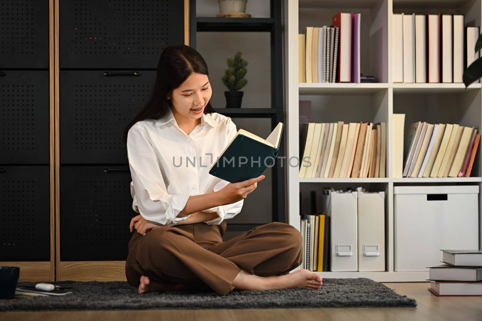 Full length of young woman wearing casual clothes reading book, spending free spare time at home.