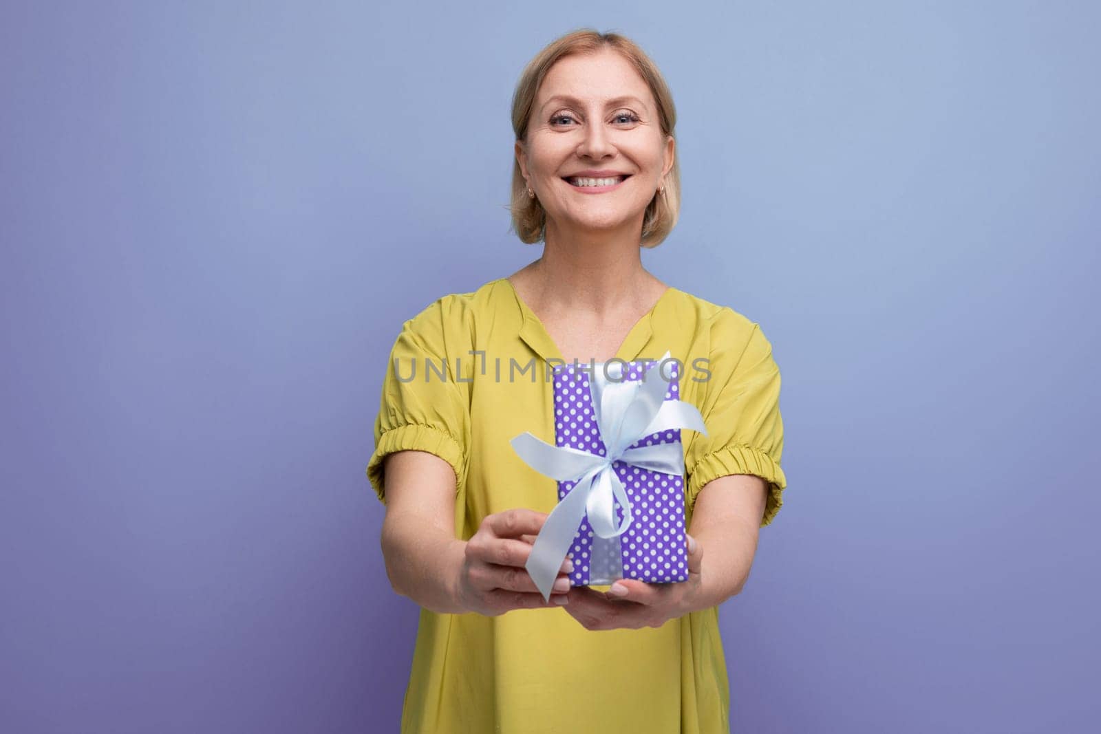 smiling blonde 50s woman holding out a gift box with a bow for a surprise.