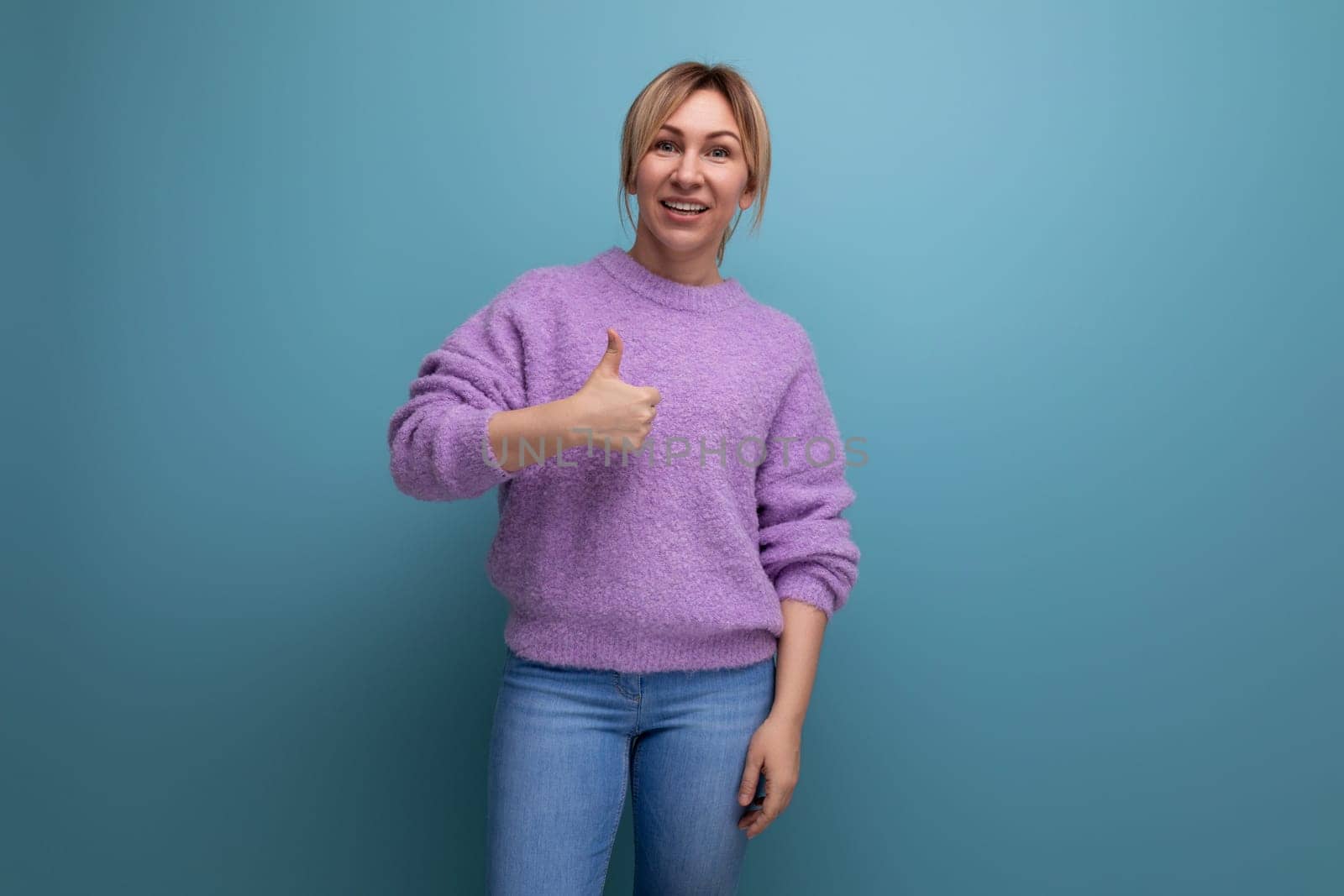 nice cute blond young woman consultant in purple sweater showing super class thumbs up on blue background with copy space by TRMK