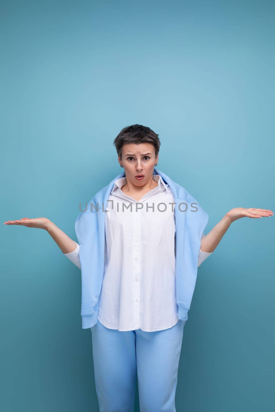 indignant surprised brunette woman with short haircut in white shirt on studio background.
