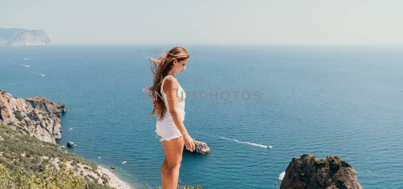 Woman travel sea. Young Happy woman in a long red dress posing on a beach near the sea on background of volcanic rocks, like in Iceland, sharing travel adventure journey