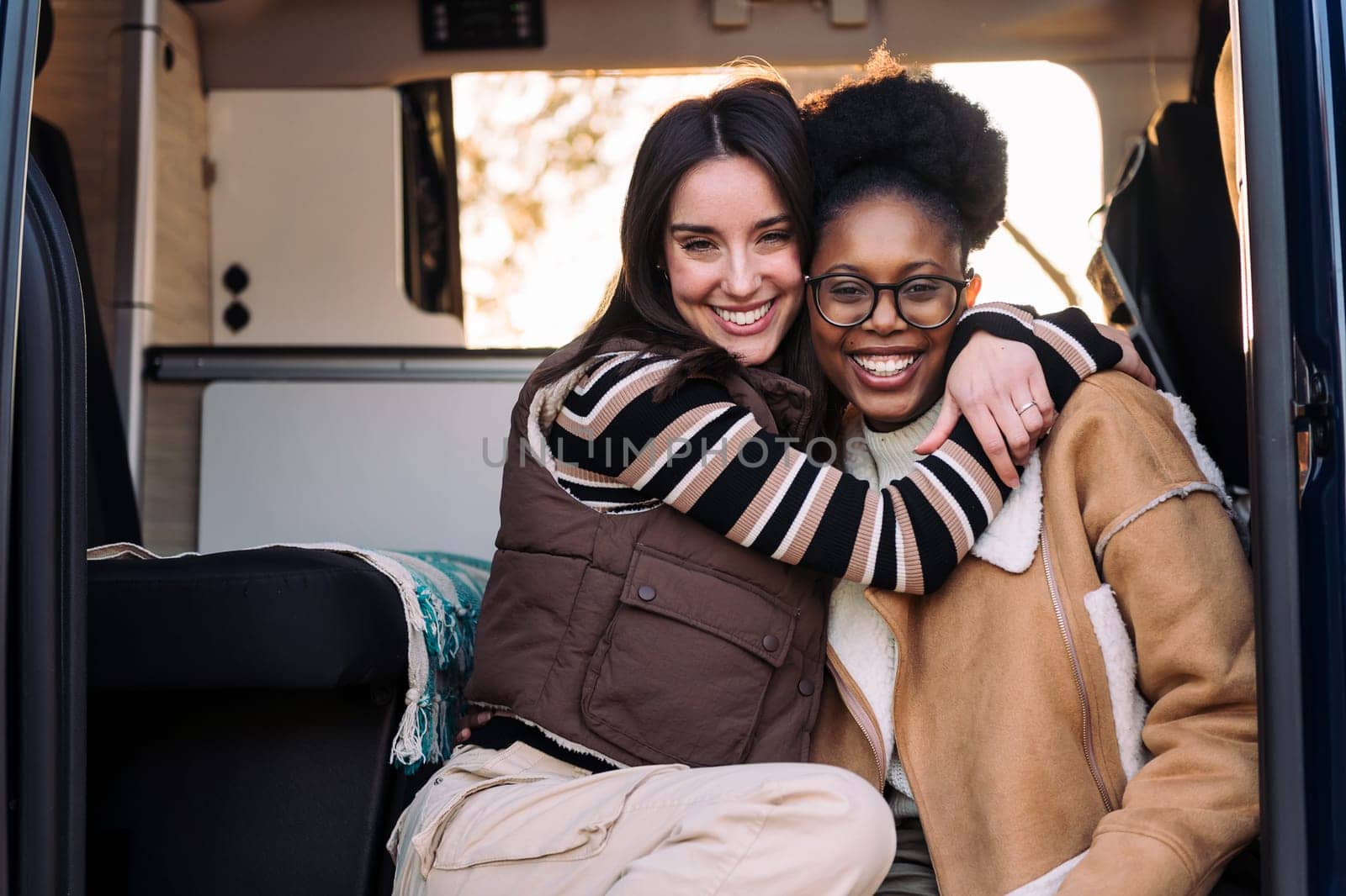 portrait of two happy women in a camper van embracing and smiling looking at camera, concept of weekend getaway and female friendship, copy space for text