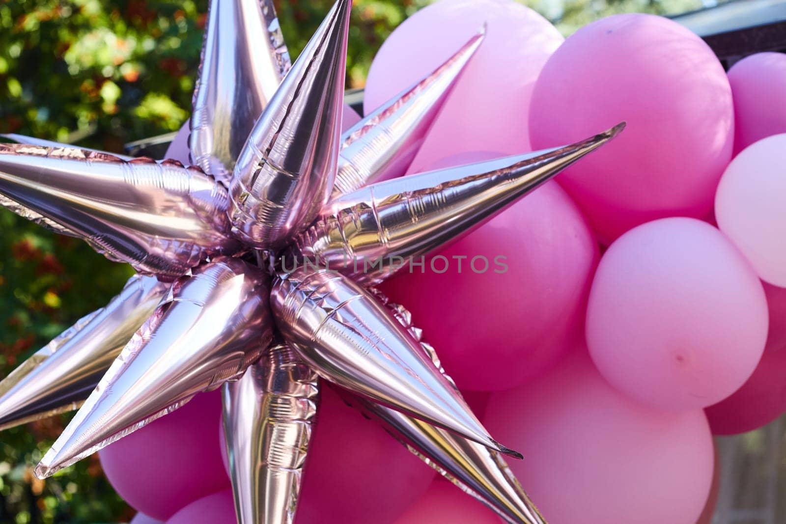Pink foil star on the background of pink balloons. Balloon arch. Birthday celebration in nature.