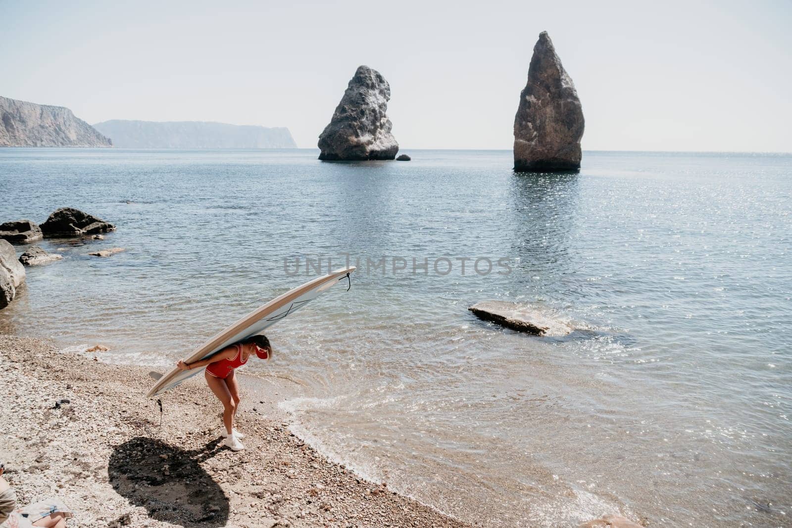 Close up shot of beautiful young caucasian woman with black hair and freckles looking at camera and smiling. Cute woman portrait in a pink bikini posing on a volcanic rock high above the sea