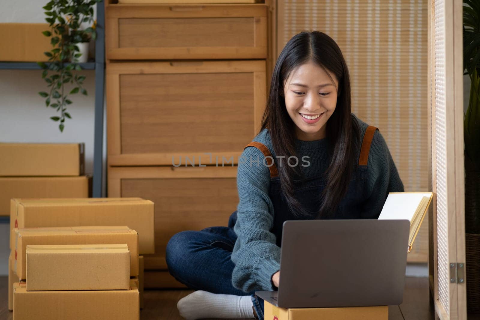 startup small business SME, Entrepreneur happy owner hold book looking at laptop and write customer address on the box for delivery. High quality photo