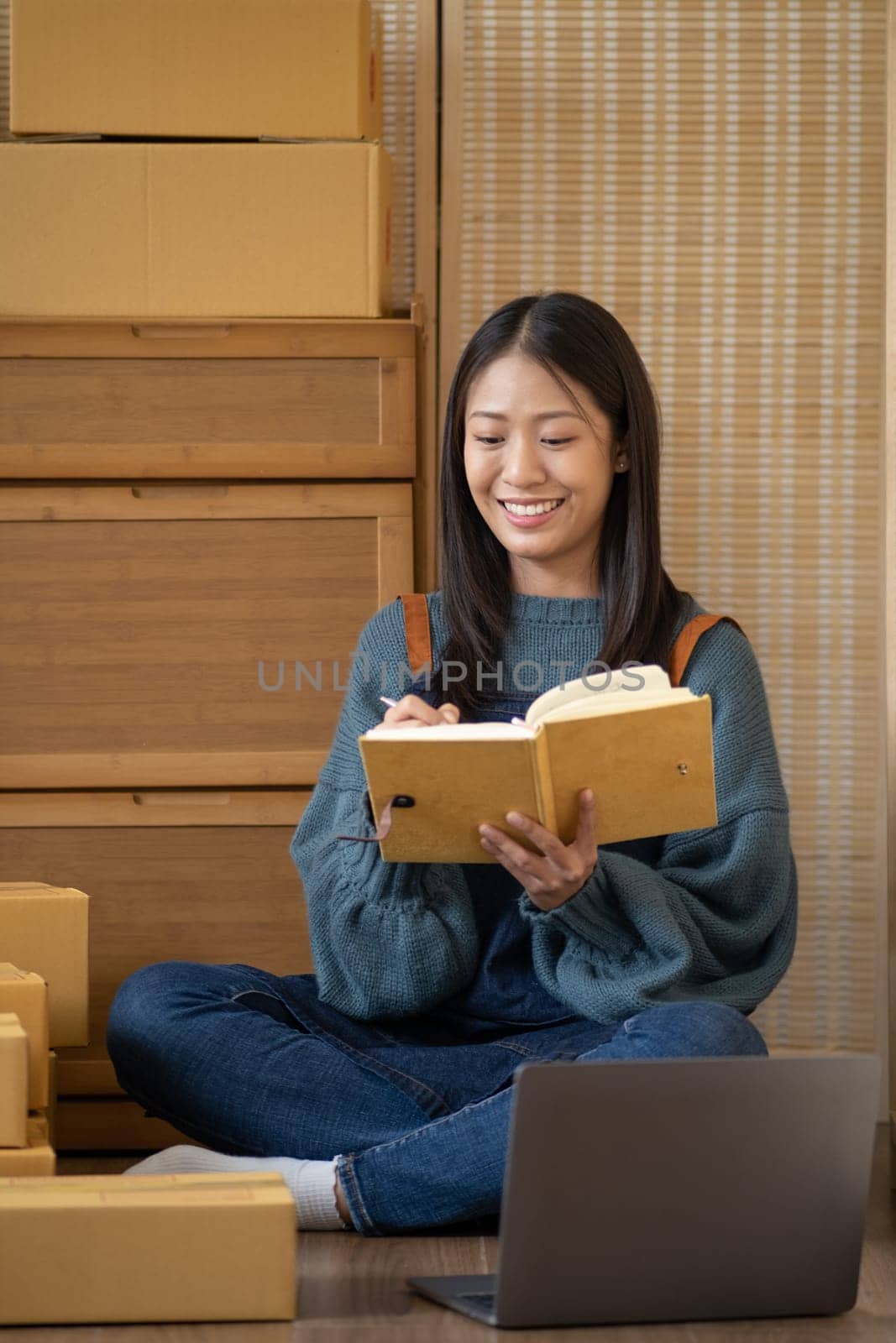 startup small business SME, Entrepreneur happy owner hold book looking at laptop and write customer address on the box for delivery. High quality photo