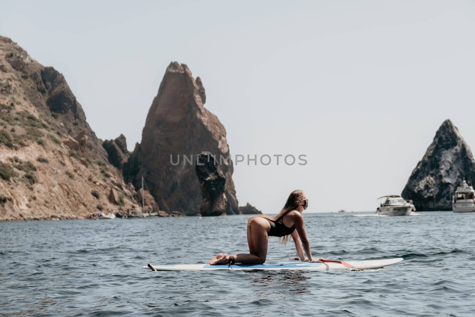 Close up shot of beautiful young caucasian woman with black hair and freckles looking at camera and smiling. Cute woman portrait in a pink bikini posing on a volcanic rock high above the sea