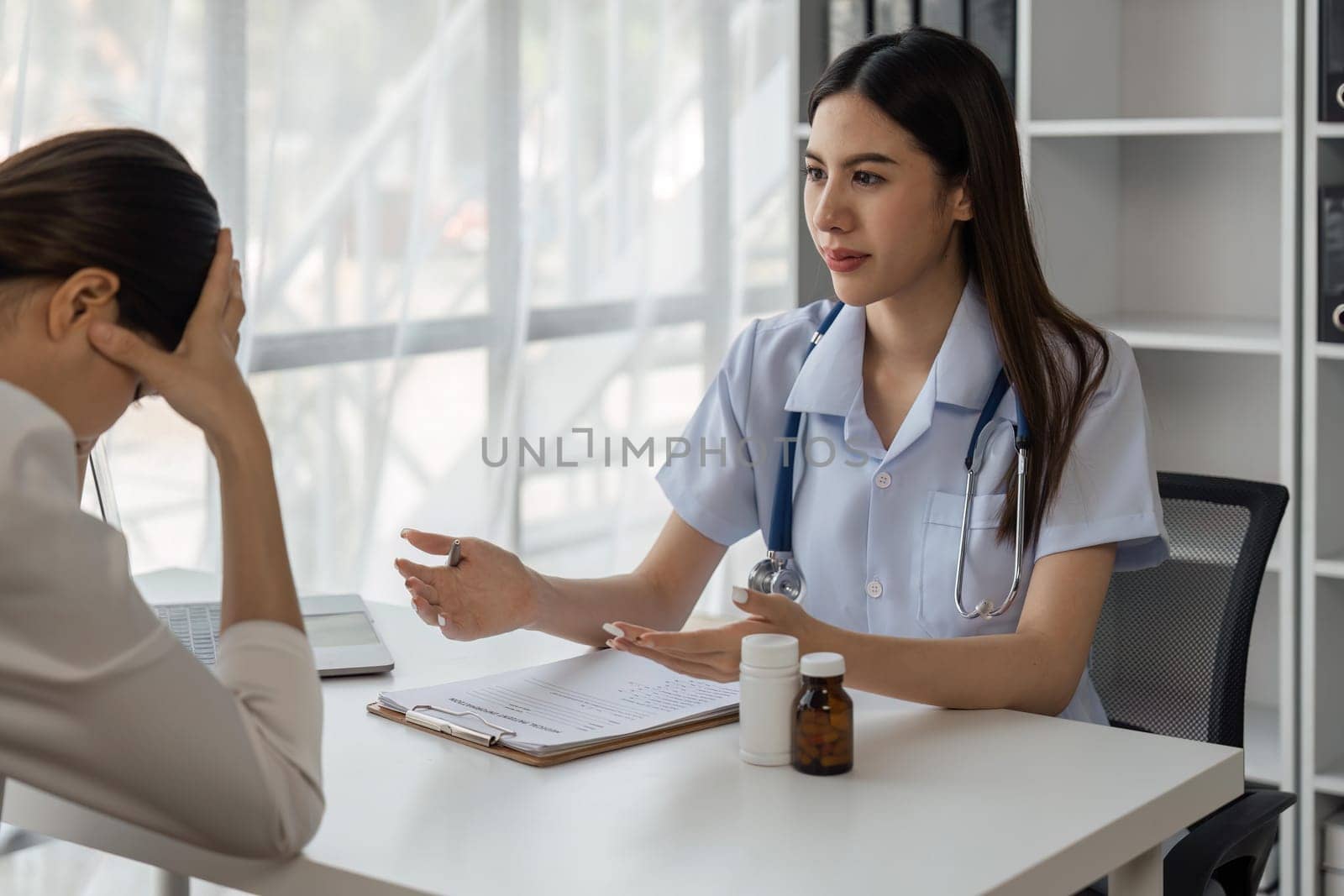Serious female doctor in medical discussion discussing results or symptoms with stressed female patient in hospital by nateemee