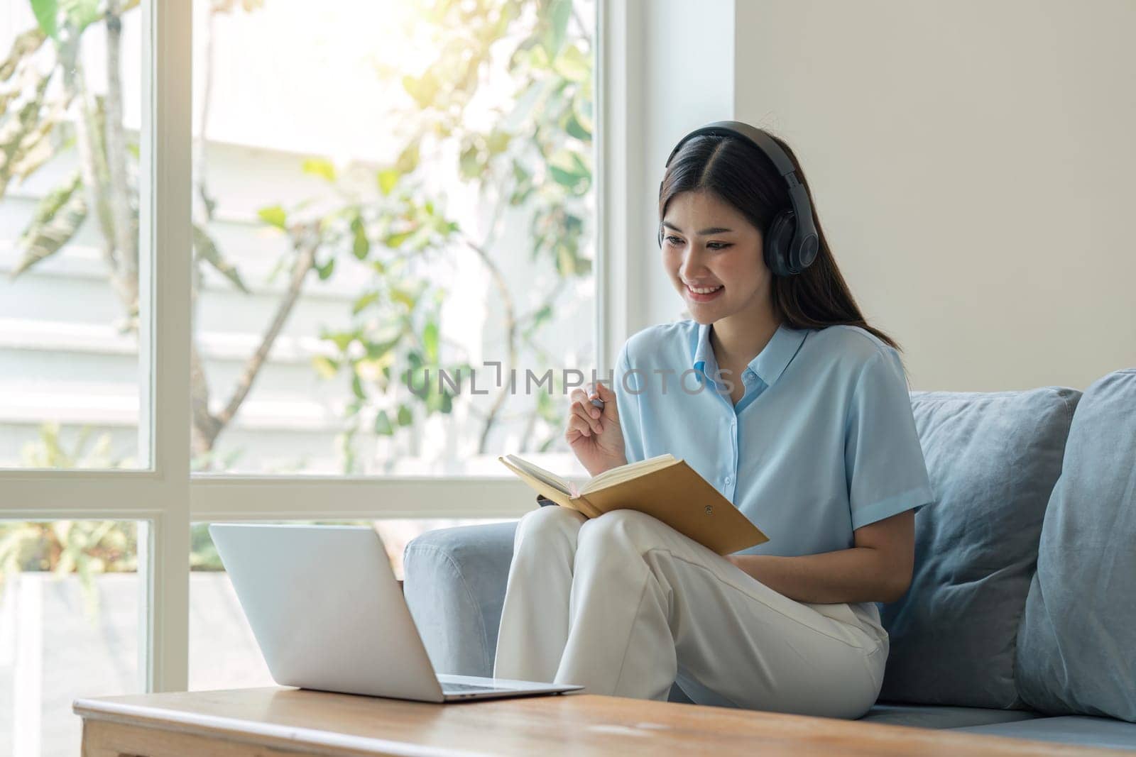 young woman working on laptop and taking notes while listening to lecture at home.