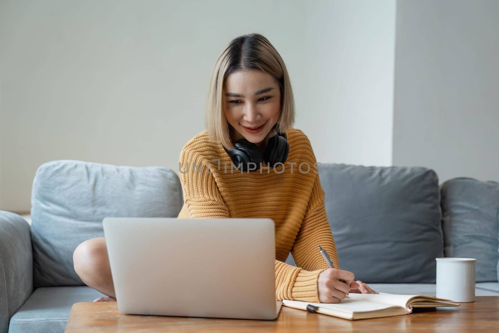 young woman working on laptop and taking notes while listening to lecture at home.