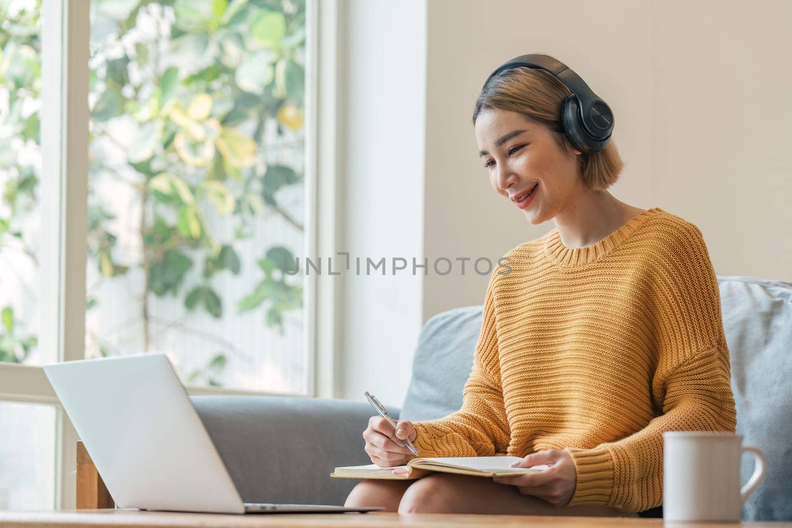 young woman working on laptop and taking notes while listening to lecture at home.