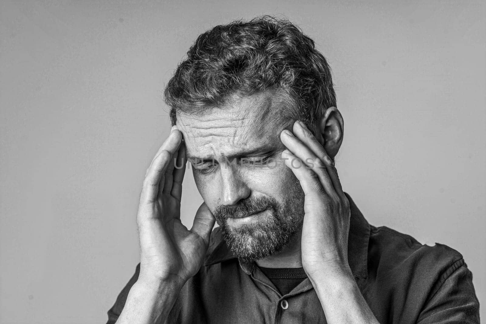Man who appears to be in pain, holding his face with two hands against a plain white background. The image captures the expression of discomfort and suffering on the mans face. by LipikStockMedia