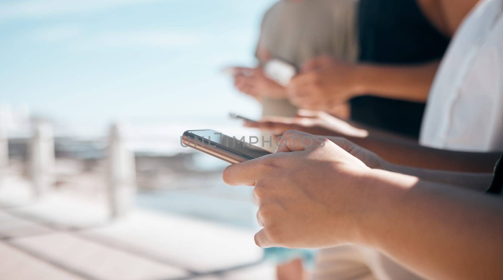 People, hands and phone in networking at beach chatting, texting or social media together in the outdoors. Hand of group on smartphone for communication, typing or data sharing mobile app on mockup.